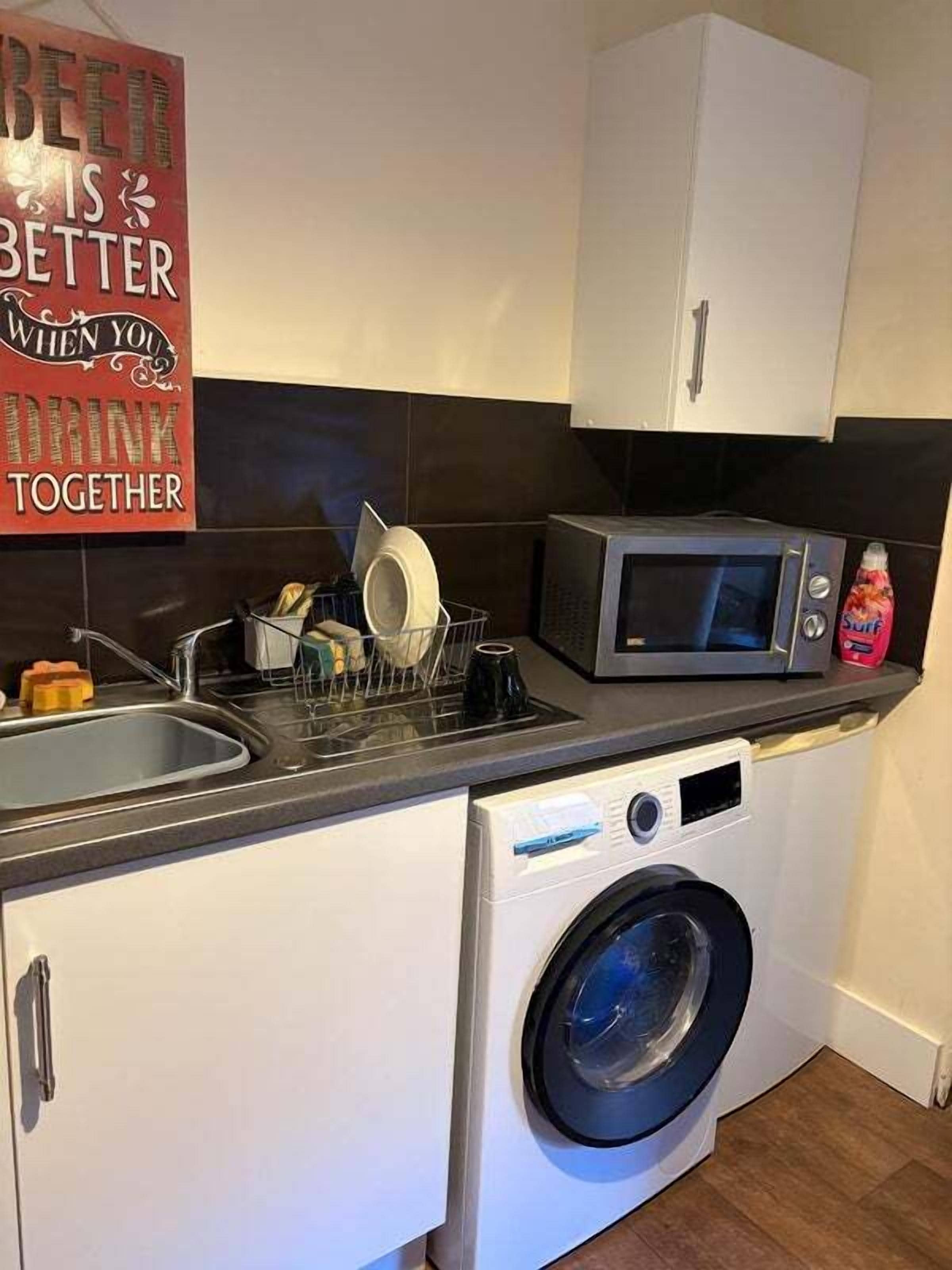 A compact kitchen with a microwave, a washing machine, and a dish rack.