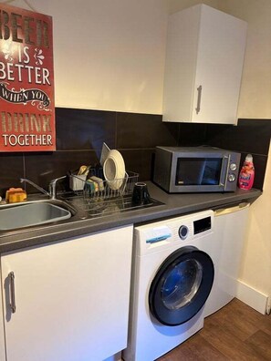 A compact kitchen with a microwave, a washing machine, and a dish rack.