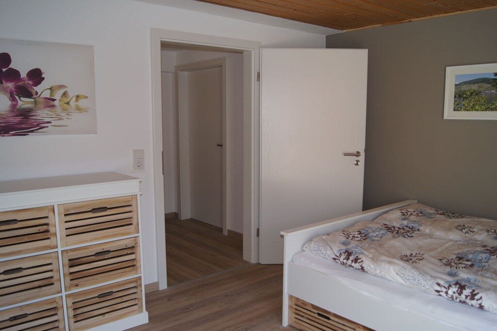 Een slaapkamer met een bed, houten opbergmeubels, een deur en een schilderij aan de muur.