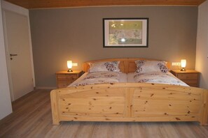 A bedroom with a wooden bed, two bedside tables with lamps, a framed picture on the wall, and a door to the left. - Holiday apartment with 2 bedrooms (Bernkastel-Andel)
