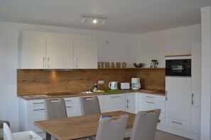 A modern kitchen with white cabinets, a wooden countertop, and a dining table with chairs. - New building with dune views (Juist)