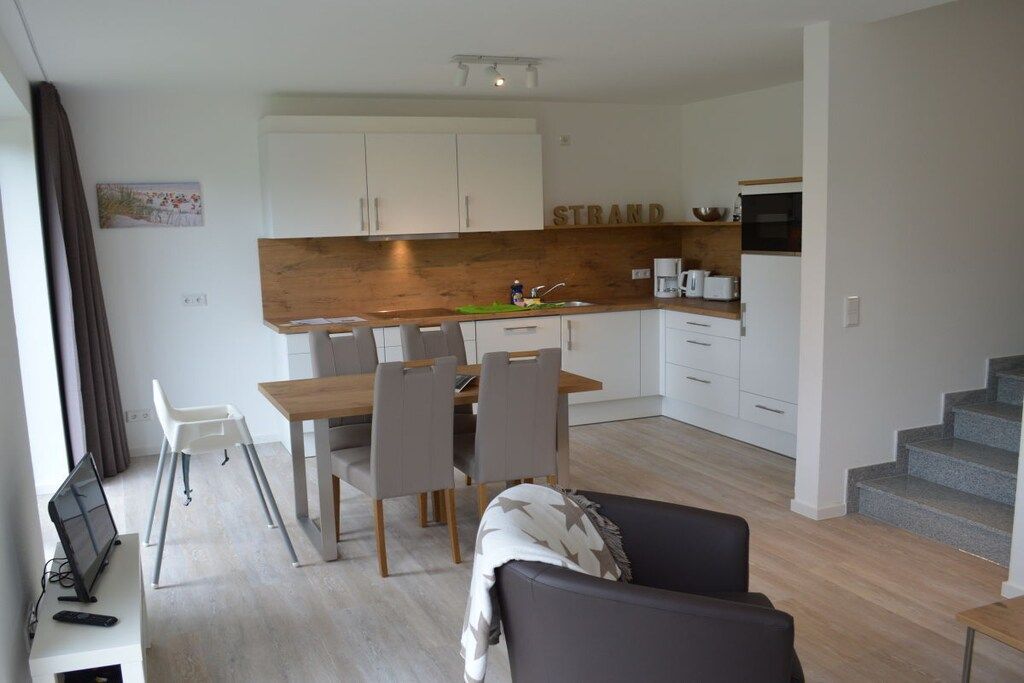 A modern kitchen with white cabinets, a wooden countertop, and a dining area with a table and chairs.