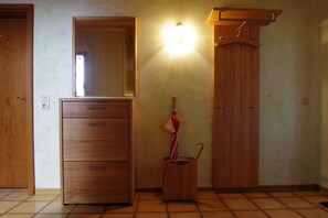 A room with a wooden cabinet, a mirror, a wall-mounted light, and a wooden shoe rack. - Holiday apartment with 1 bedroom (Pottum)