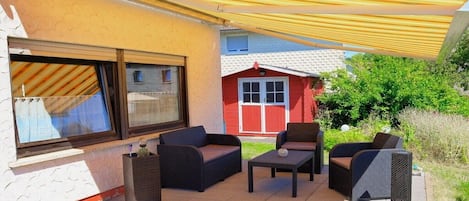 An outdoor patio with wicker furniture, a table, and a yellow awning.