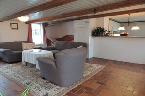 Ein Wohnzimmer mit einer Sofagarnitur, einem kleinen runden Tisch und einer Küchenzeile inklusive Theke und Pendelleuchten.