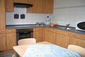 A compact kitchen with wooden cabinets, a built-in oven, a microwave, and a small dining table with chairs. - Holiday home in the North Sea with 1 bedroom (Cuxhaven-Sahlenburg)