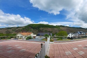 A residential area with a paved terrace, houses with solar panels, and a hilly landscape in the background. - ||-----------------------Erdener Steps----------------------|| (Erden)