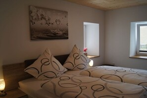 Ein Schlafzimmer mit Bett, Kissen, einem Nachttisch, einem Wandbild, einem Fenster und einem Beistelltisch mit Lampe.