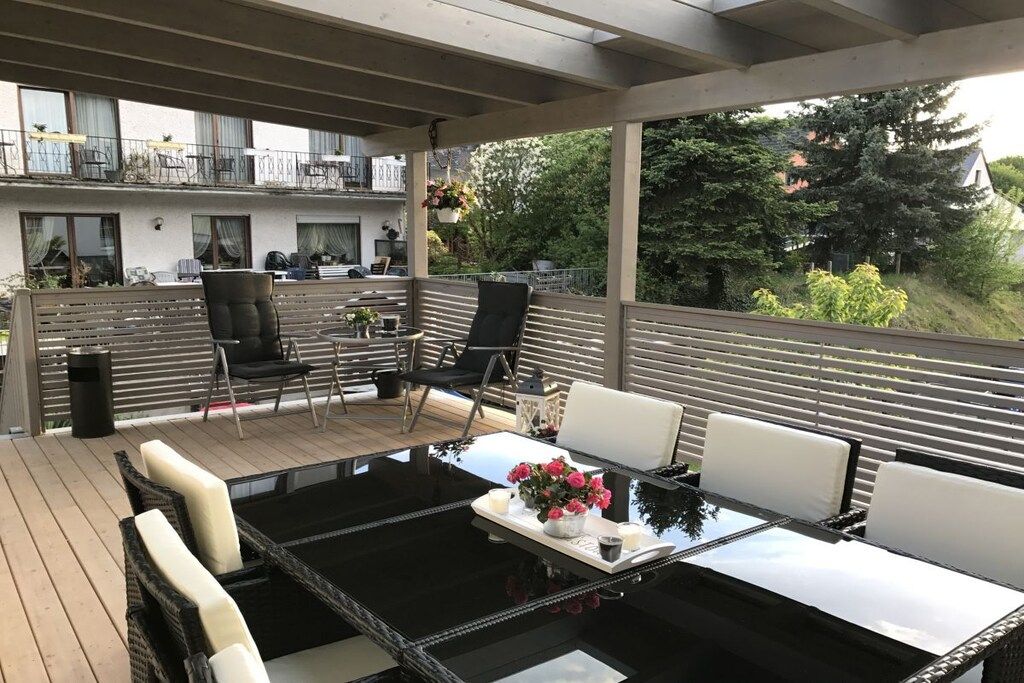 An outdoor patio with a glass-top table, white and black chairs, and a small table with flowers and candles.