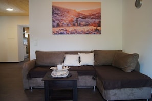 Ein Wohnzimmer mit einem braunen Sofa, einem kleinen Tisch mit Kerze und Snacks sowie einem Wandbild einer Winterlandschaft.