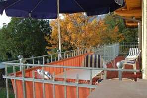 A covered outdoor seating area with a metal railing, a table, and two striped chairs. - Heller Holiday Winery (Traben-Trarbach \/ Wolf)