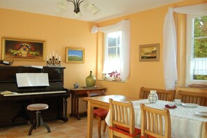A room with a piano, dining table, chairs, and artwork on the walls. - Heller Holiday Winery (Traben-Trarbach \/ Wolf)
