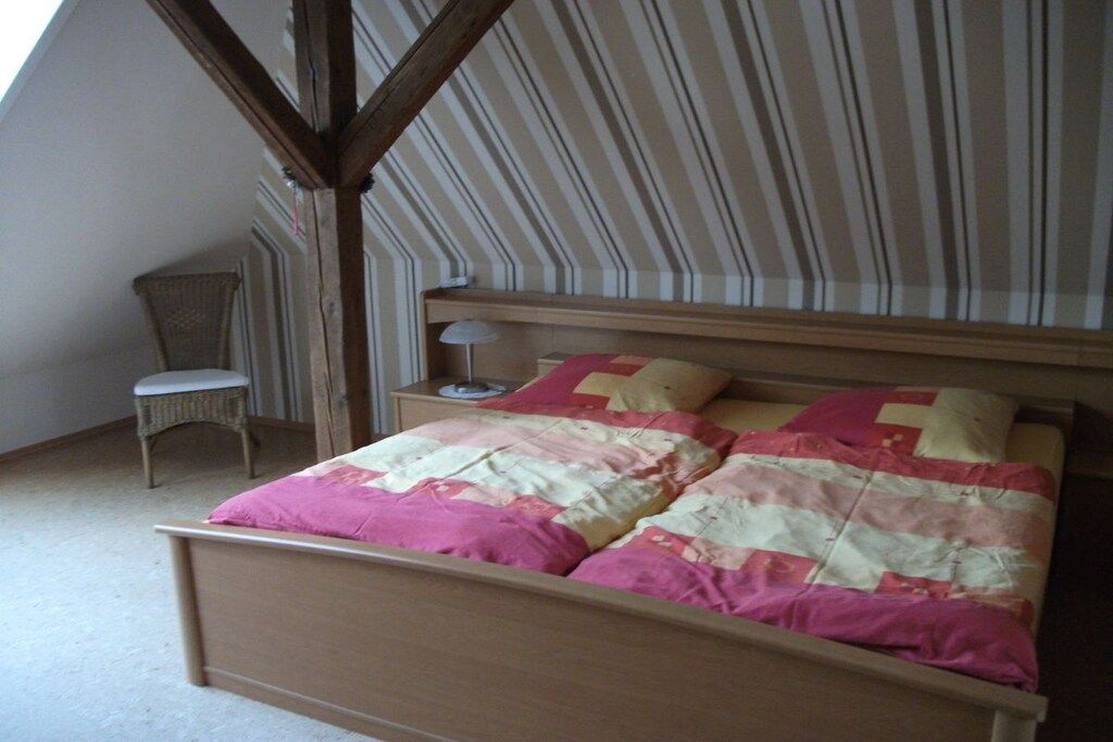 Un dormitorio con cama, mesita de noche, lámpara, silla y ventana.