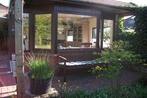 Ein überdachter Außenbereich mit Sitzbank, einem Blumentopf und Blick auf ein Haus durch eine Glastür.
