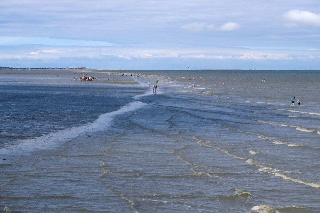 Ein Strand mit Menschen, die am Ufer entlanggehen, und einem Boot in der Ferne.