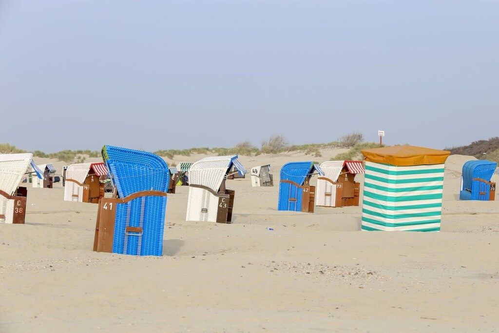 Des cabanes de plage, chacune portant un numéro sur sa porte, disposées en rangées sur une plage de sable.