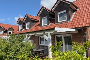 A residential building with a red-tiled roof, multiple windows, and a patio area with a table and chairs. - Holiday home in Borkum with swimming pool (Borkum)