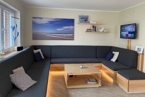 A modern living room with a sectional sofa, a coffee table, and a flat-screen TV. - Holiday home in Borkum with swimming pool (Borkum)