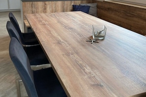 Une table à manger en bois avec des chaises, un récipient en verre décoré d’une étoile de mer et un banc en bois avec des coussins.
