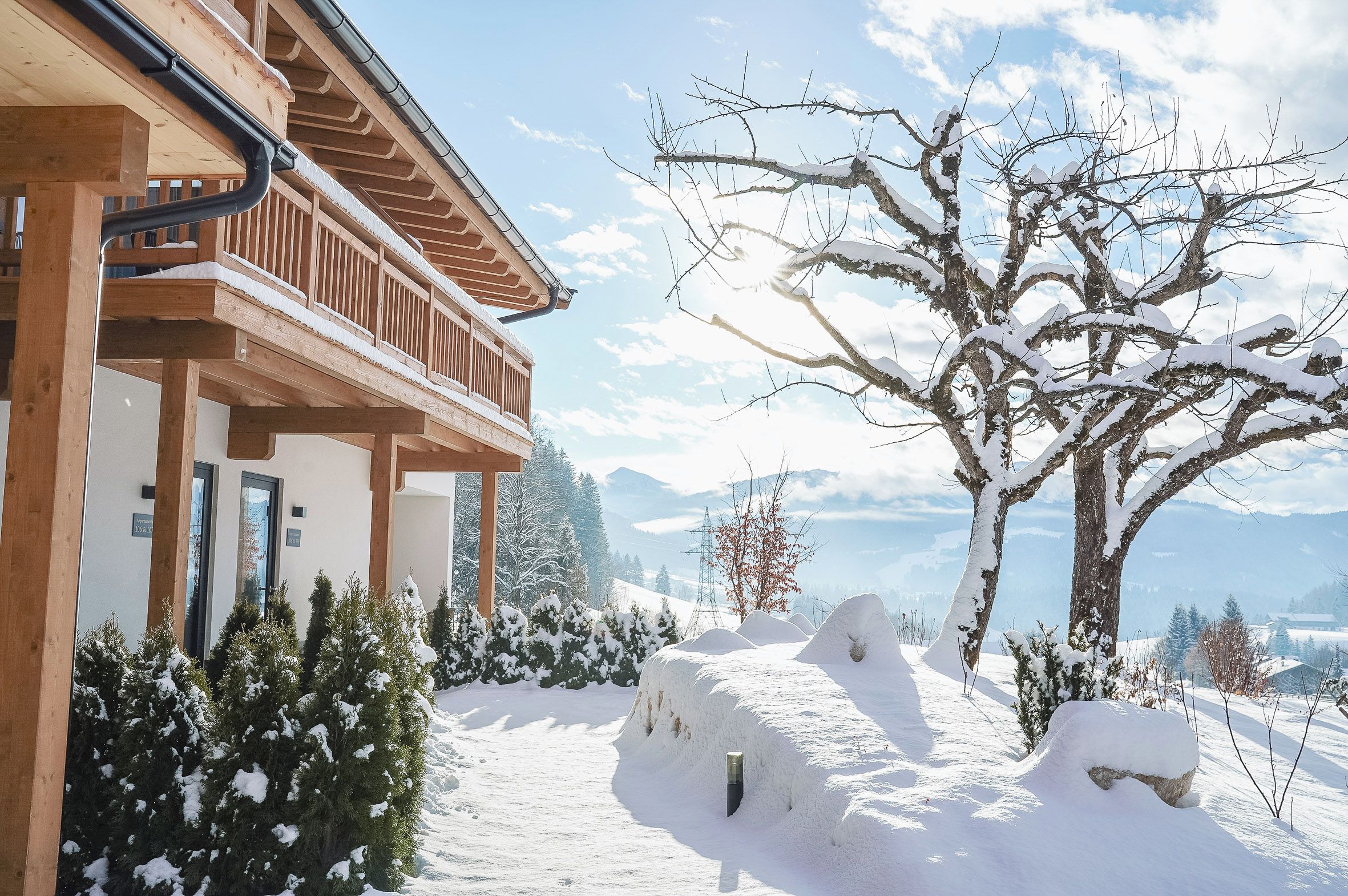 A wooden building with a balcony, surrounded by snow-covered trees and a clear sky.