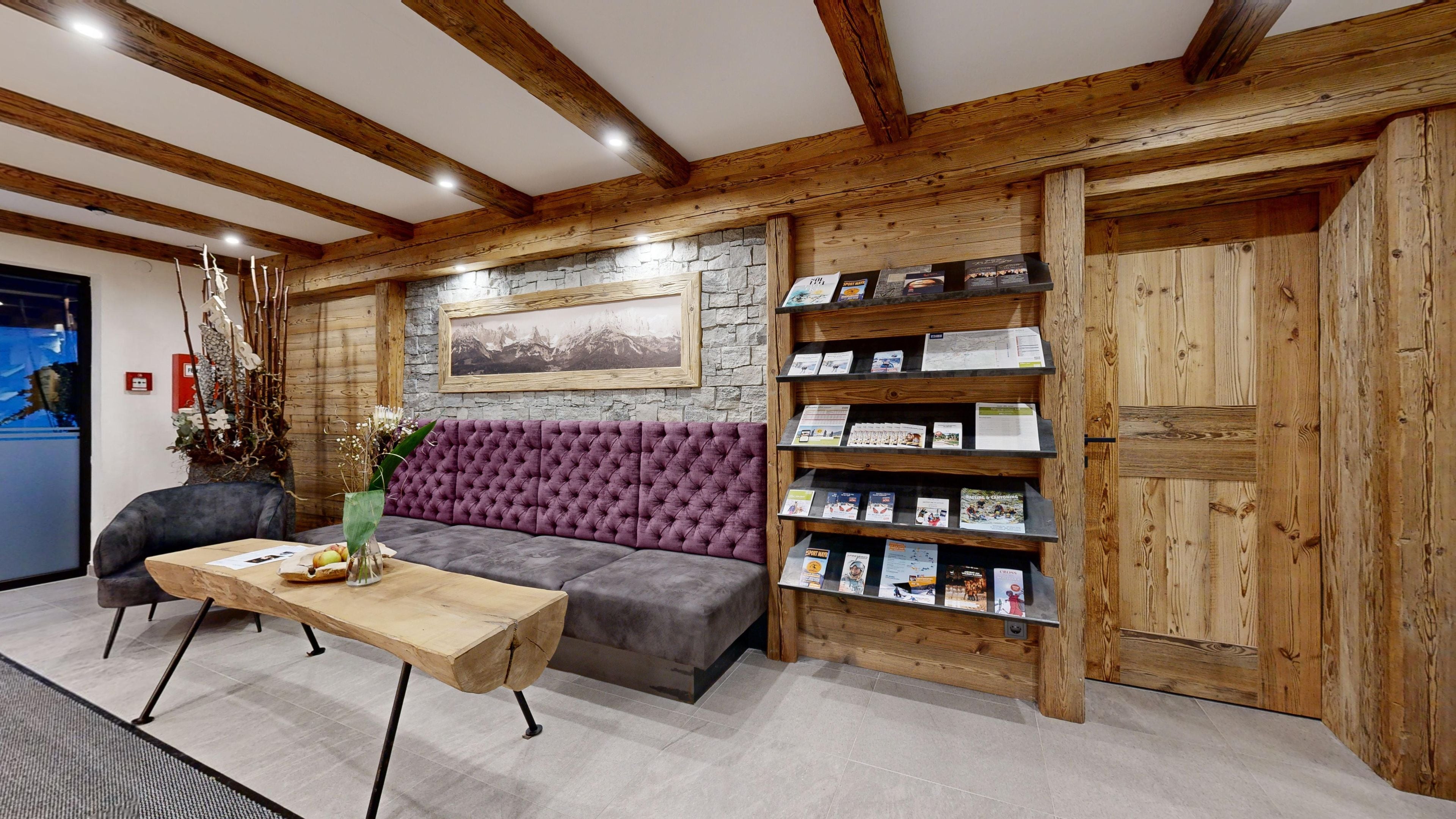 Ein Empfangsbereich mit Holzboden, einer Steinwand, einem violetten Sofa, einem Holztisch und einem Bücherregal mit Broschüren.