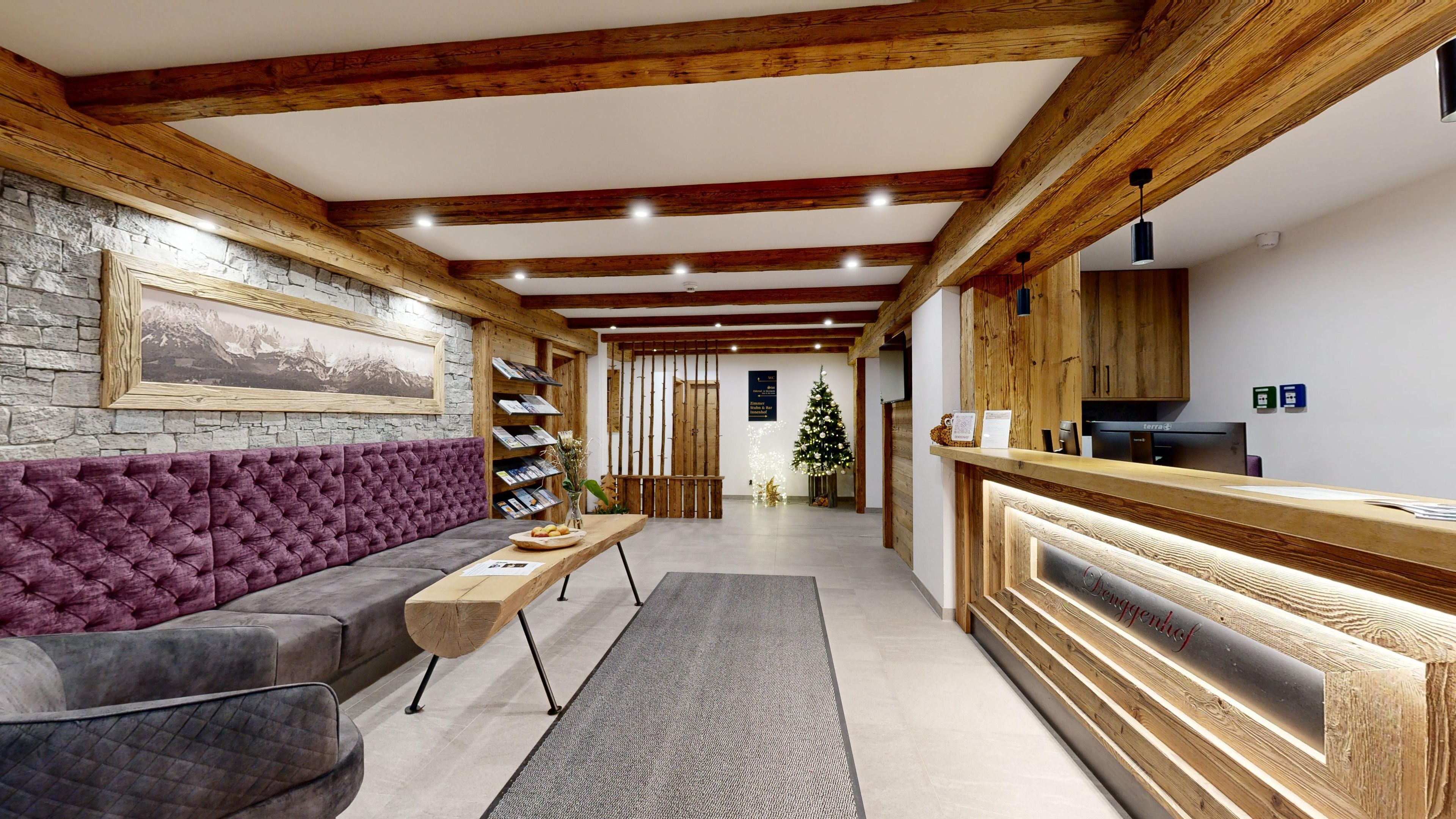 Un espace d’accueil comprenant un comptoir de réception en bois, un canapé, une table basse et un sapin de Noël.