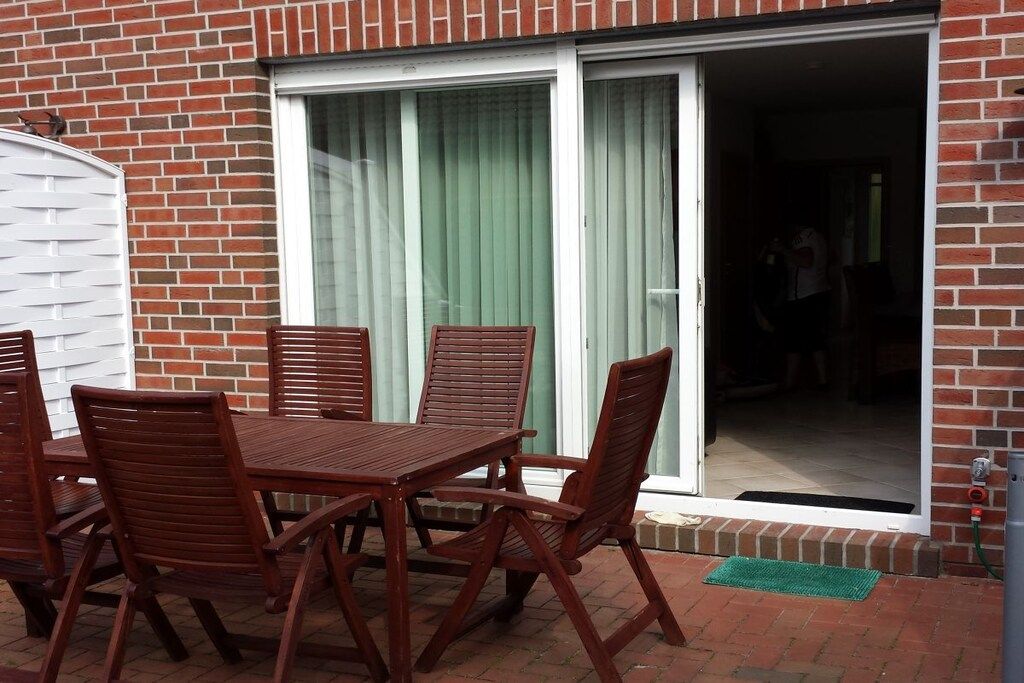 A patio with a table and chairs, a sliding glass door, and a brick wall.