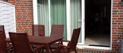 A patio with a table and chairs, a sliding glass door, and a brick wall.