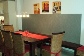 A dining area with a table and chairs, a red placemat, and wall art depicting social scenes. - Holiday home in Borkum with swimming pool (Borkum)