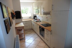 A kitchen with white cabinets, a wooden countertop, a built-in oven, and a window providing natural light. - Holiday home in Borkum with swimming pool (Borkum)
