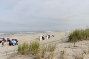 A beach with beach chairs and umbrellas, a lifeguard station, and a sandy path leading to the water. - Holiday Residence Oystercatcher I/No. 1 (Spiekeroog)