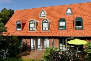 A red-roofed building with multiple windows and a covered porch area. - Holiday Residence Oystercatcher I/No. 1 (Spiekeroog)