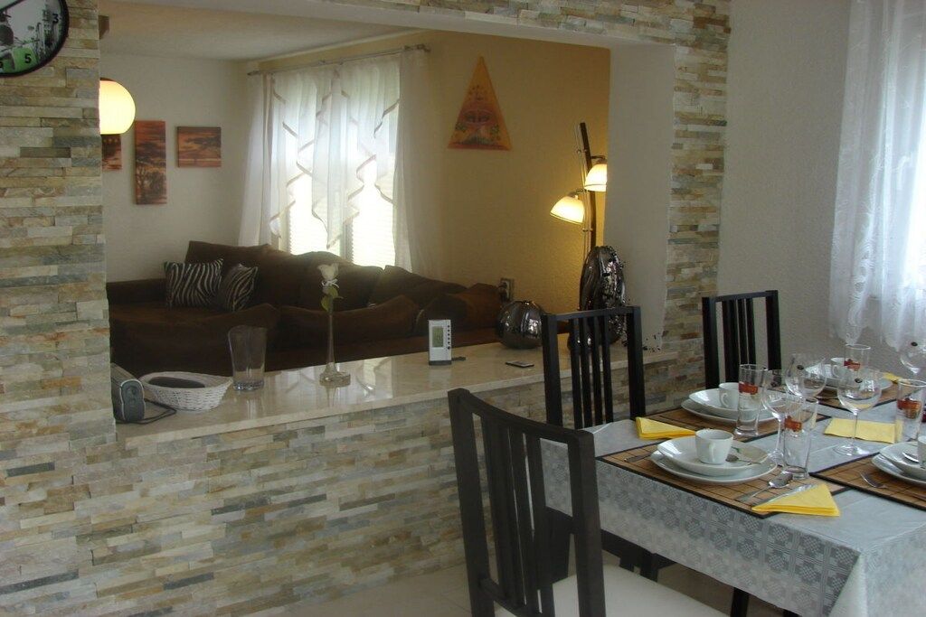 Un comedor con pared de piedra, un sofá al fondo y una mesa para dos personas con platos, vasos y cubiertos.
