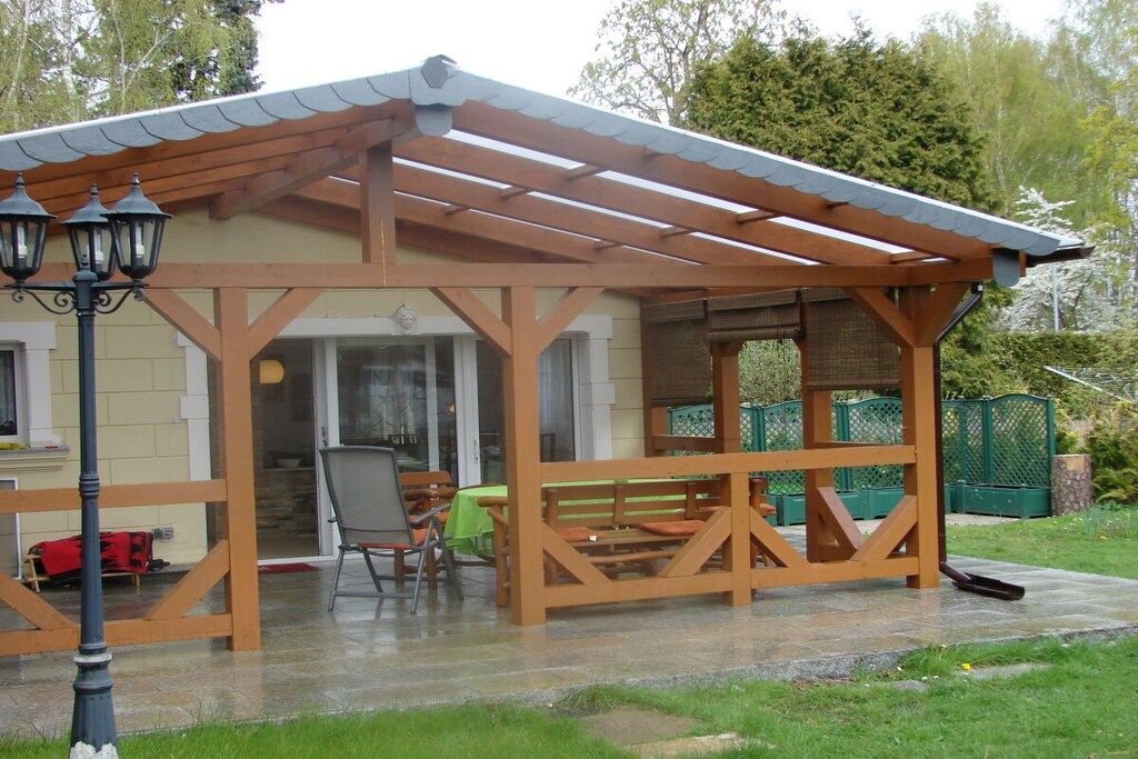 A covered outdoor seating area with a wooden pergola, a bench, and a table.
