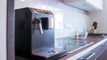 Een moderne keuken met een ingebouwde koffiemachine, een eettafel met glazen blad en roestvrijstalen apparatuur.