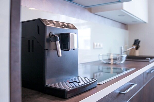 Een moderne keuken met een ingebouwde koffiemachine, een eettafel met glazen blad en roestvrijstalen apparatuur.