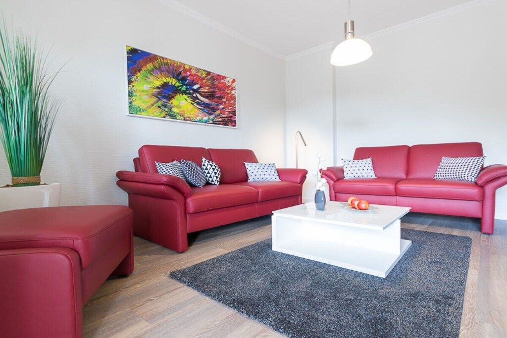 Een moderne woonkamer met twee rode banken, een witte salontafel en een kleurrijk abstract schilderij aan de muur.