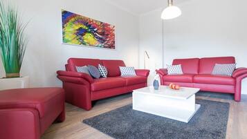Een moderne woonkamer met twee rode banken, een witte salontafel en een kleurrijk abstract schilderij aan de muur.