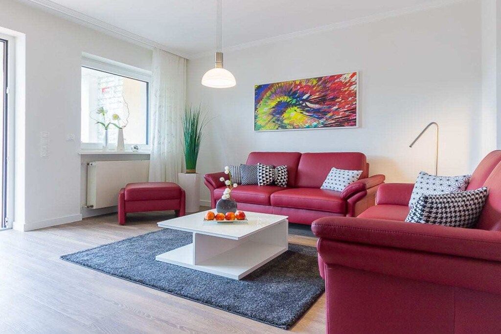A modern living room with a red sofa set, a white coffee table, and a colorful abstract painting on the wall.