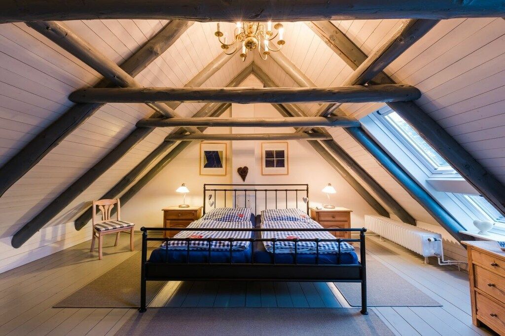 An attic bedroom with a sloped ceiling, a central bed, two bedside tables, a radiator, and a chandelier.