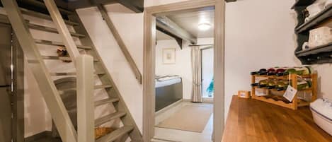 Una escalera conduce a un dormitorio con cama y ventana. A la derecha, una estantería con botellas de vino.