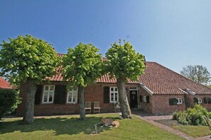 Un bâtiment en briques surmonté d’un toit de tuiles rouges, avec une pelouse et deux arbres.