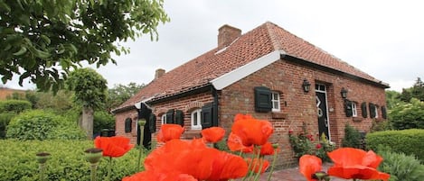 Una casa de ladrillo con techo de tejas, rodeada por un jardín con amapolas rojas.