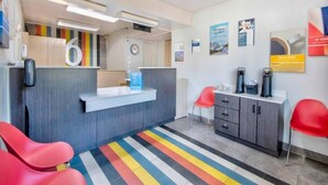 Zona de recepción con mostrador, sillas, máquina de café y una alfombra a rayas de colores.