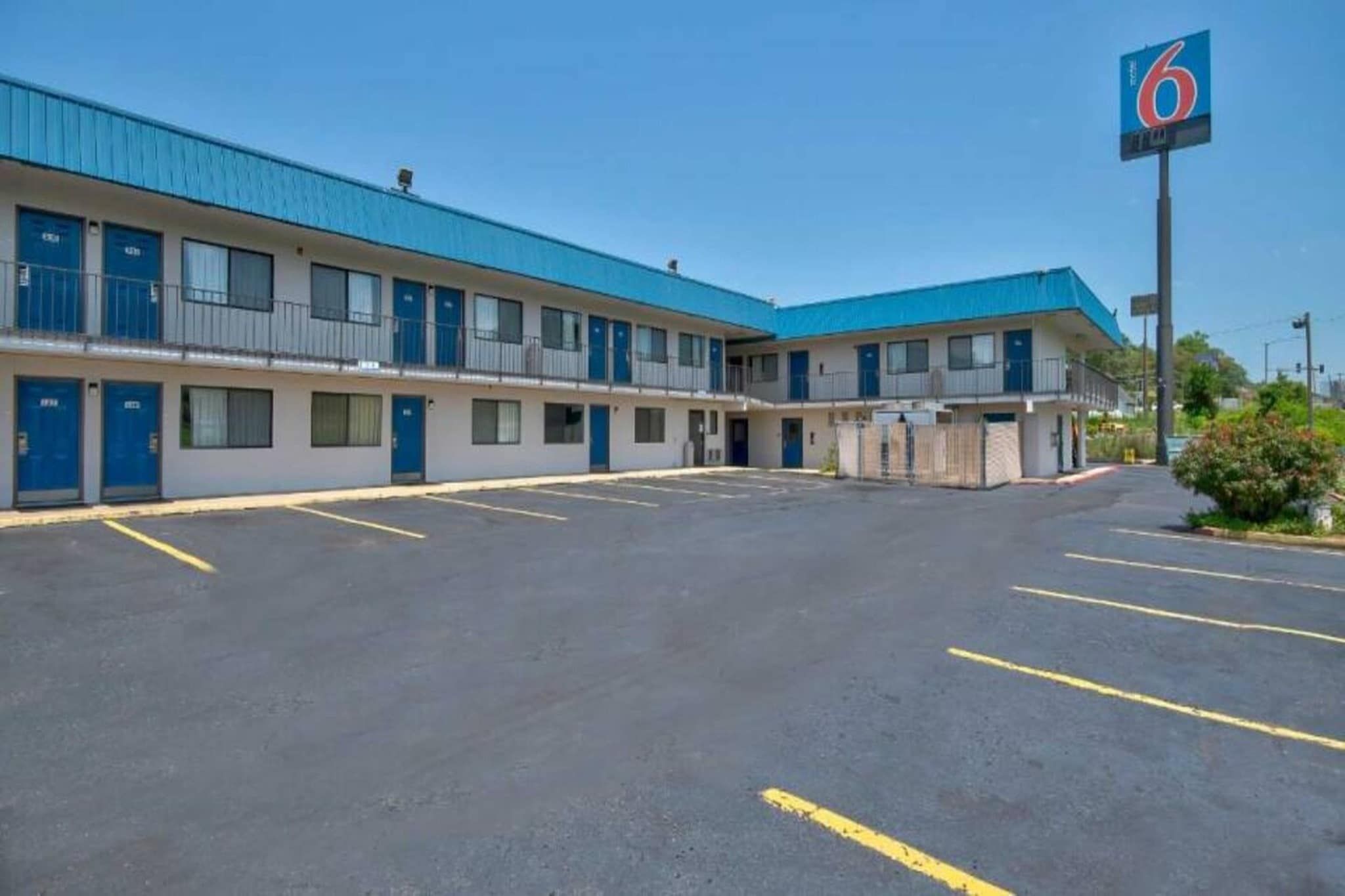 A motel with a blue roof and multiple rooms, a parking lot, and a sign indicating the number 6.