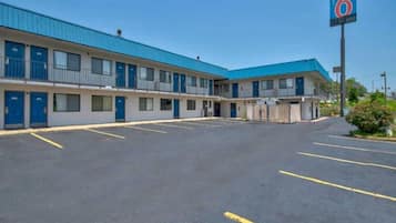 A motel with a blue roof and multiple rooms, a parking lot, and a sign indicating the number 6.