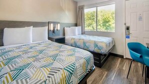 Habitación de hotel con dos camas, un escritorio, una silla y una ventana con vistas a árboles.