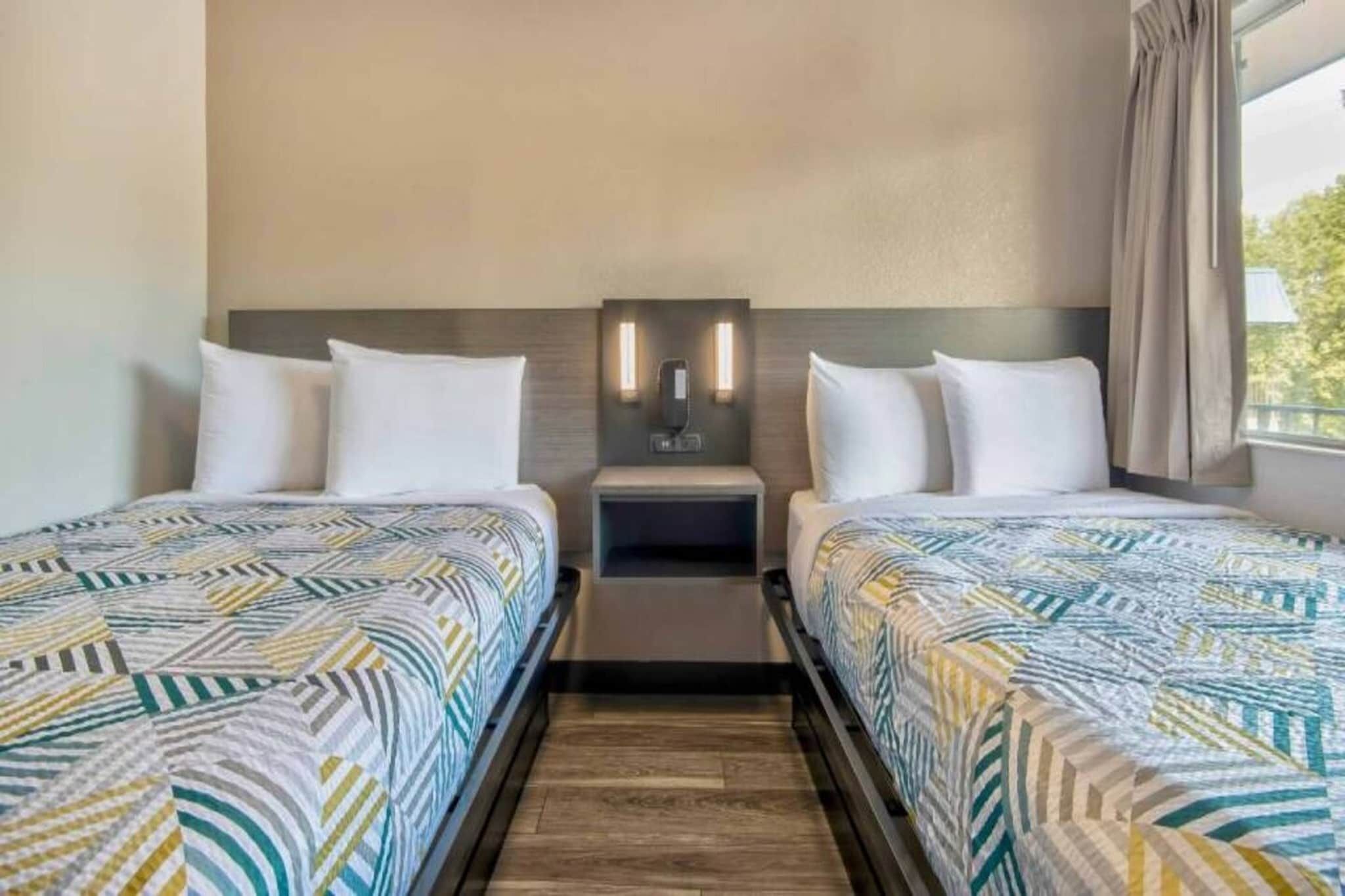 Una habitación de hotel con dos camas, una mesita de noche y una lámpara de pared.