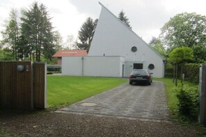 Un bâtiment moderne doté d’un toit triangulaire original, d’une allée pavée et d’une voiture garée.