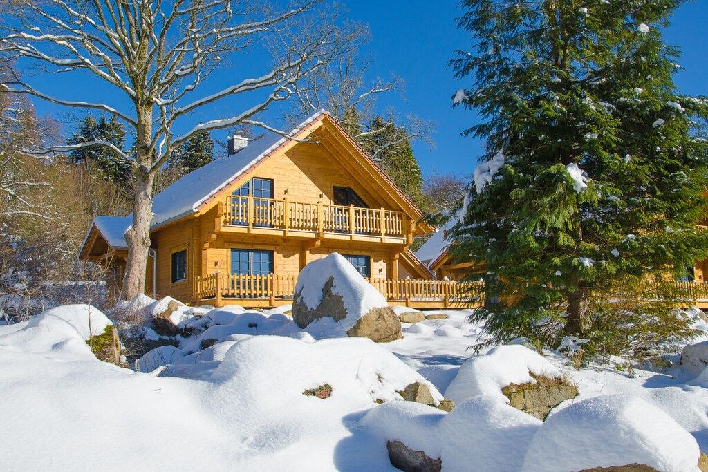Eine Holzhütte mit einem Balkon, umgeben von verschneitem Gelände und Bäumen.